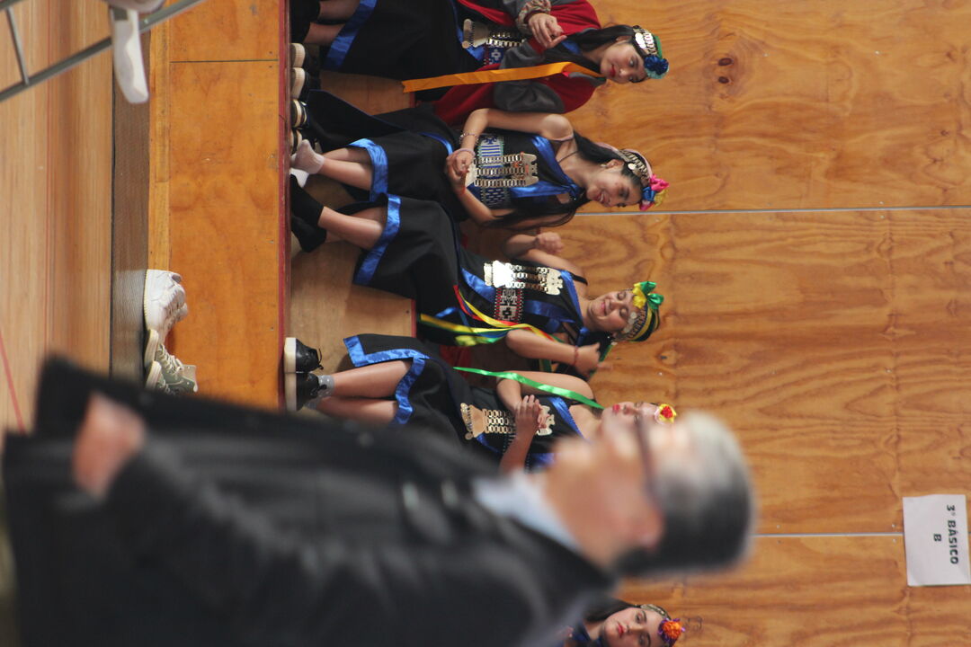 Estudiantes participando en una actividad sobre el escenario decorado con motivos culturales