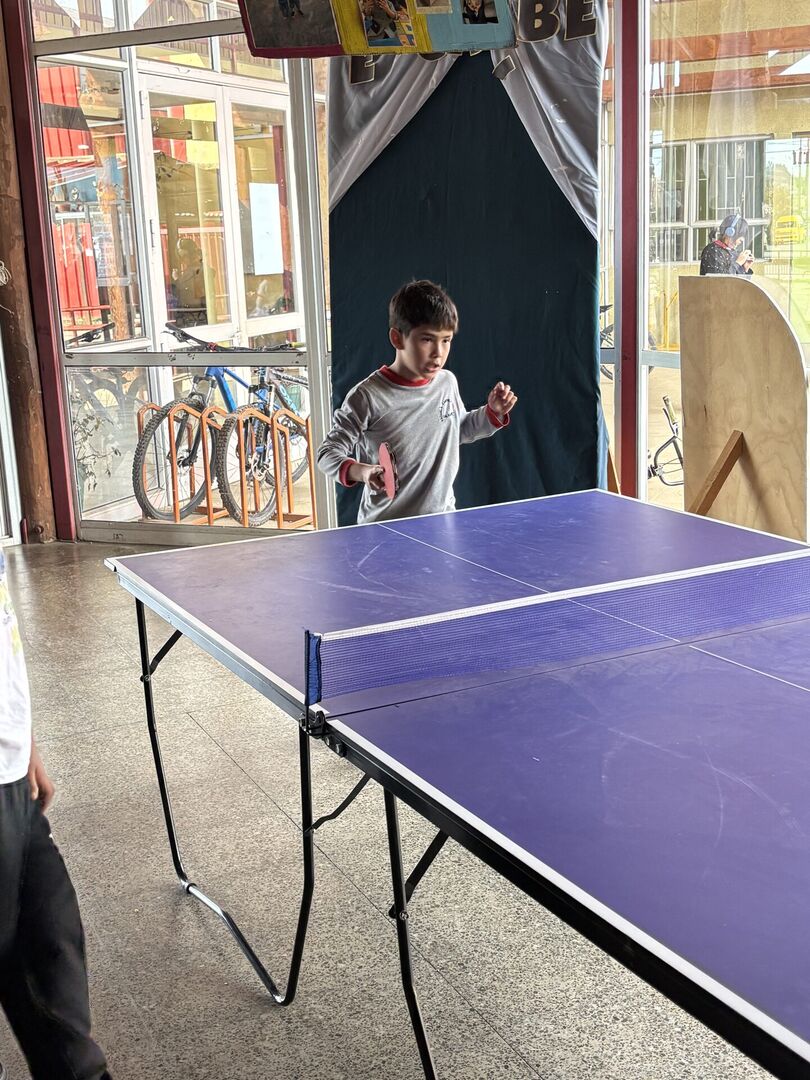 Grupo de estudiantes posando juntos con paletas de ping pong frente a un mural escolar