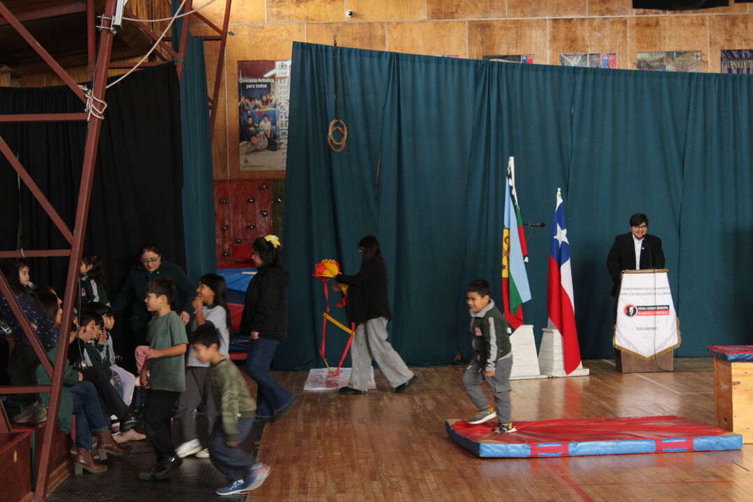 Plano amplio del escenario con bandera mapuche, bandera chilena y atril institucional del DAEM Galvarino